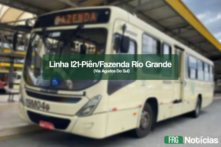 Um ônibus de transporte coletivo de cor creme, estacionado em um terminal coberto. No centro da imagem, há um retângulo verde semitransparente com o texto em branco: Linha I21-Piên/Fazenda Rio Grande (Via Agudos Do Sul). No canto inferior direito, aparece o logotipo FRG Notícias. O fundo mostra a estrutura metálica do terminal e outros veículos de forma desfocada.