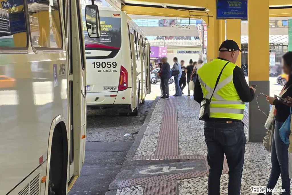 Imagem ilustrativa com a vista de um terminal de transporte metropolitano em Curitiba, com um ônibus da linha 'H01 Araucária-Guadalupe' estacionado. Em primeiro plano, um funcionário de colete refletivo observa a movimentação, e ao fundo, passageiros aguardam na plataforma, ilustrando a operação do sistema de transporte monitorado pela AMEP.