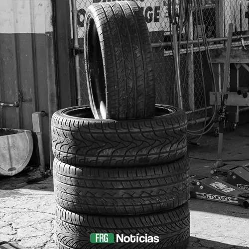 Fotografia em preto e branco de cinco pneus empilhados em um ambiente de oficina. Na base da imagem, o selo FRG Notícias.