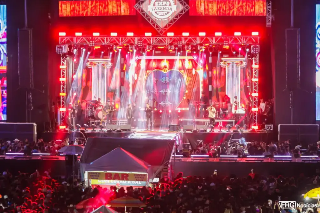 Palco principal da Expo Fazenda em Fazenda Rio Grande com show ao vivo, iluminação cênica vermelha, grande público e logomarca do evento ao centro.